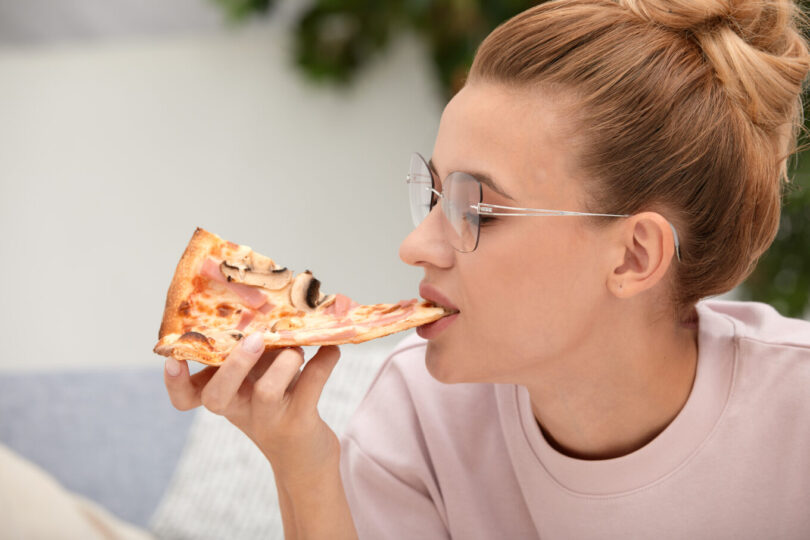 Close-up face of blond woman in glasses eating piece of pizza. Kako se pravilno jede pizza: vodič za savršeno uživanje u omiljenom jelu